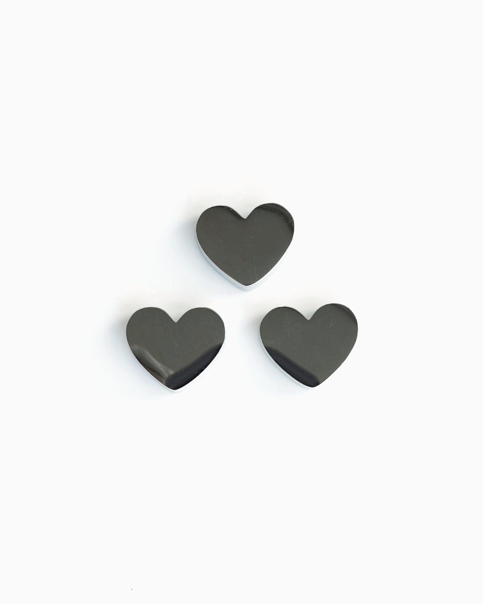 Three heart-shaped stainless steel matcha sifter charms arranged together on a pale grey background