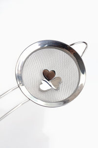Three heart-shaped stainless steel charms sitting in an empty mesh matcha sifter