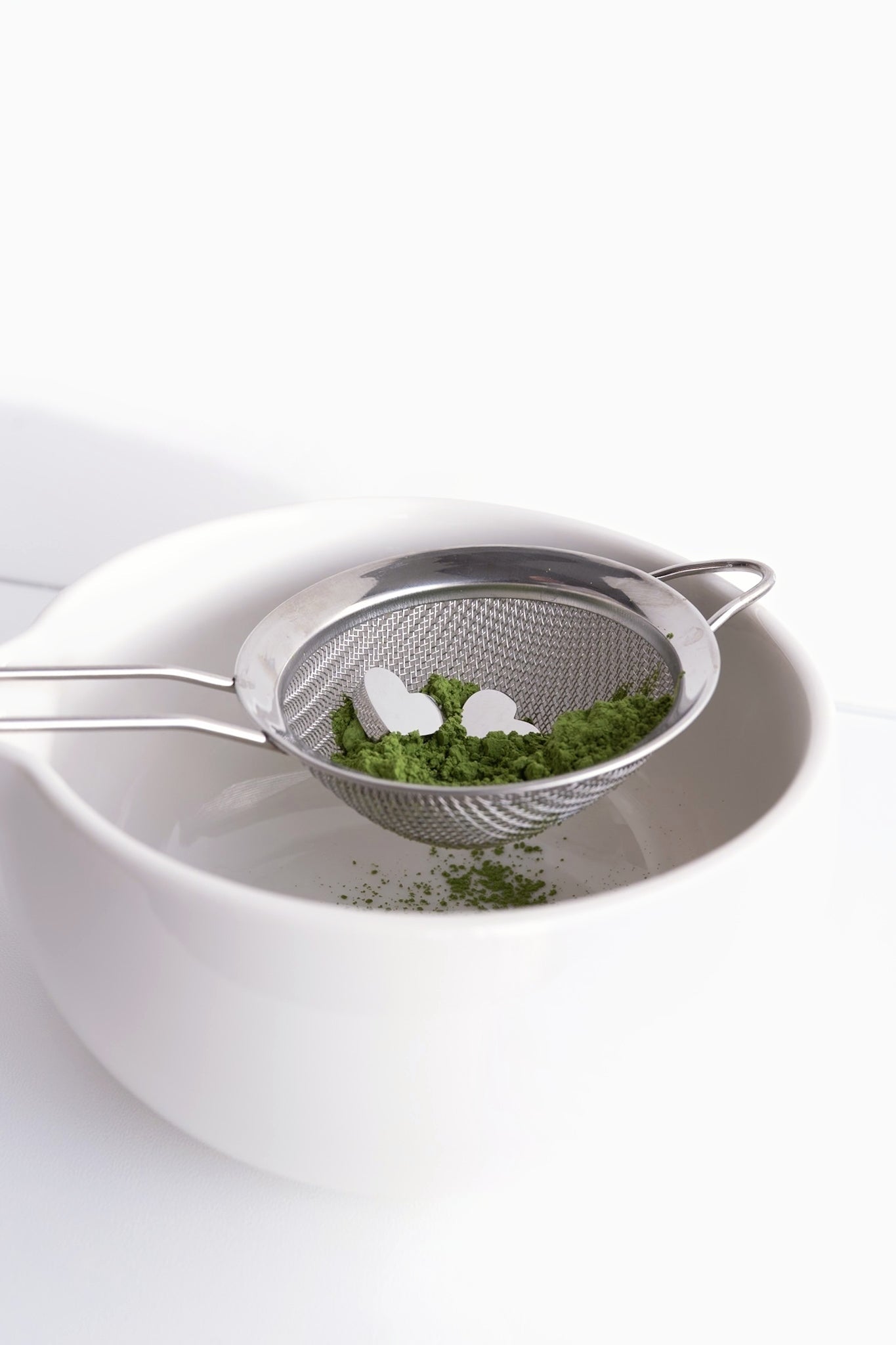 Matcha powder passing through a sifter with the heart-shaped charms as it is swirled