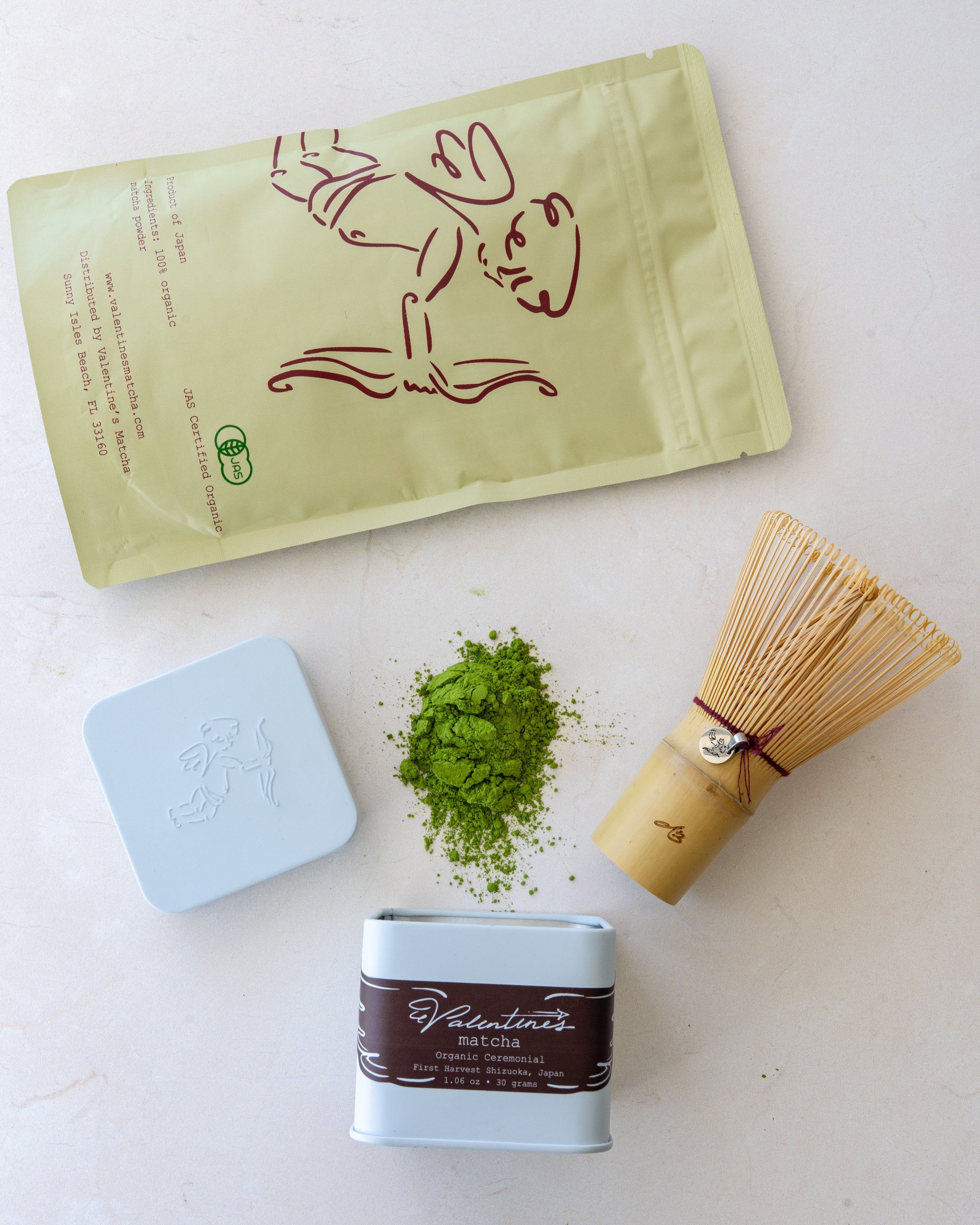 baking matcha pouch, ceremonial matcha tin, bamboo whisk, and loose matcha powder arranged on neutral background