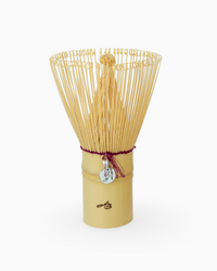 Bamboo whisk with a cylindrical handle and silver charm hanging on a white background